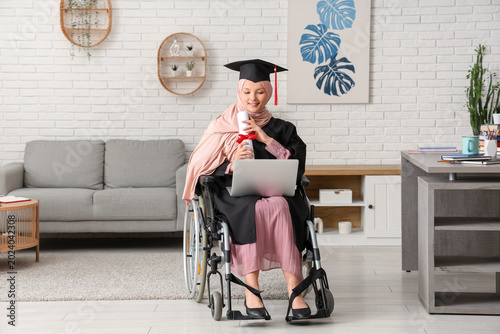 Beautiful female Muslim graduate student in wheelchair with graduation cap, l...