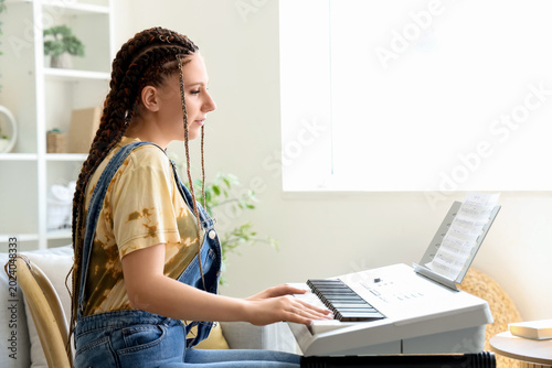 Foto Young woman with dreadlocks playing synthesizer at home