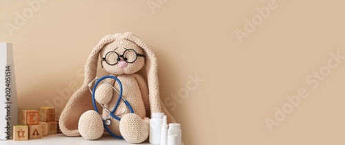 Bunny toy with stethoscope and medications on shelf against beige background ...