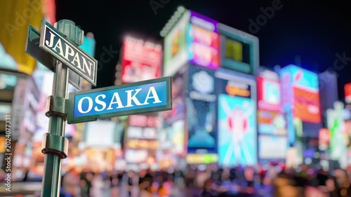 Osaka Japan Shopping District Timelapse. Selective focus of travel sign Osaka and Japan with real timelapse from raw photos . Bustling city with dazzling billboards and busy people. Iconic landmark.
