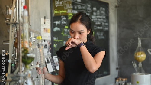 Young Asian Woman Testing Distilled Alcohol by Dropping on Hand and Smelling Aroma, Female Expert Checking Quality of Herbal Spirit in Cafe