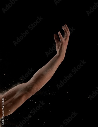 Reaching upward arm with dust particles against black background