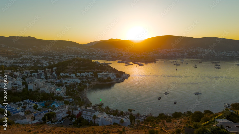 Obraz premium Bodrum, Turkey. Morning aerial drone view of Tiger Tower hill in backlight, yacht marina, yachts, Bodrum Castle and white houses. Bright sun behind mountains.. Aerial View