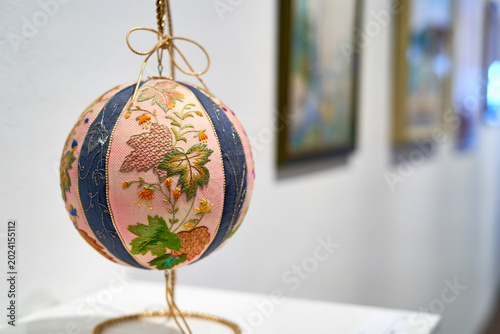 Foto A close-up shot of an intricately embroidered decorative sphere, likely a traditional Japanese temari ball, displayed on a gold wire stand