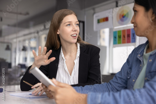 Quadro em tela Young businesswoman in formal attire lead conversation with female colleague holding digital tablet at briefing in boardroom in modern office