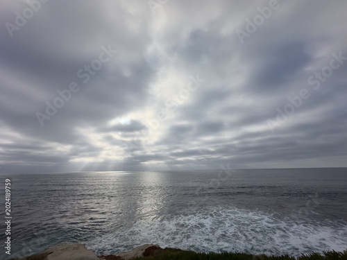 Foto Beautiful atmospheric crepuscular light rays piercing through heavy storm clouds over the vast open horizon of the Pacific Ocean in La Jolla, California