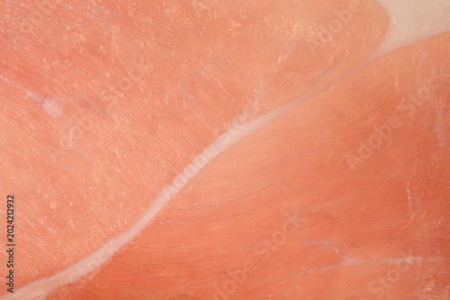 Full frame macro view of a slice of raw cured prosciutto ham showing a thin white fat line and lean pink meat texture.