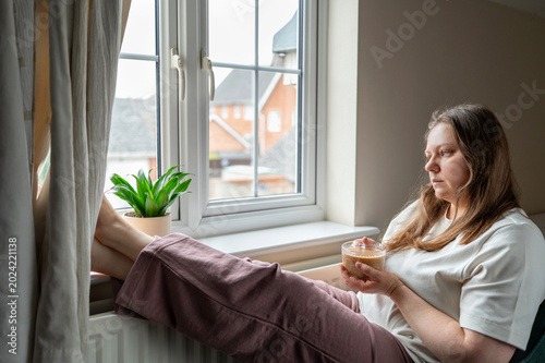 Foto Exhausted woman sitting by window with coffee at home