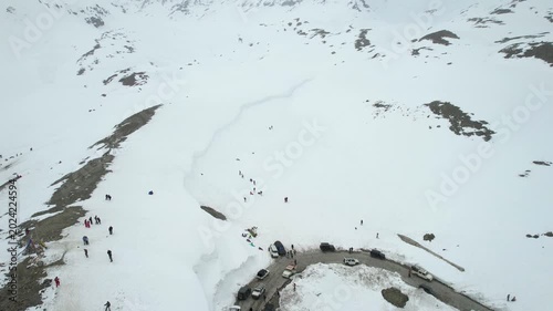 Aerial drone orbit wide view of tourists exploring snowy mountains near Shinkula Top Pass Sissu with parked 4X4 vehicles on winding roads in Ladakh Himachal Pradesh India during winter