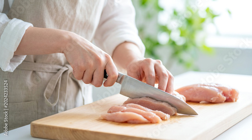 Obraz na płótnie キッチンで包丁を使い鶏肉を切る女性の手元 まな板の上で食材を調理する主婦