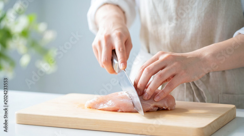 キッチンで包丁を使い鶏肉を切る女性の手元 まな板の上で食材を調理する主婦