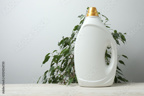Home cleaning products on a wooden table against a background of green leaves and a gray wall, space for text