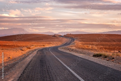 Winding empty road through a desert landscape at sunset in Morocco