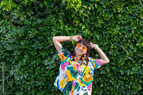 Принти на полотні A young woman wearing sunglasses and fashionable accessories stands among the green foliage of the trees
