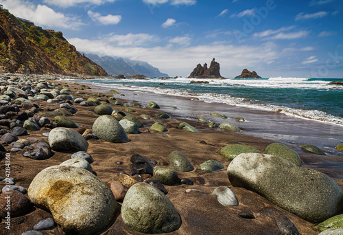 Canvastavla Dramatic shoreline with rounded stones, dark sand, sea waves, and rugged volcanic cliffs beneath, Benijo Beach in the Anaga Rural Park,  Tenerife, Canary Islands