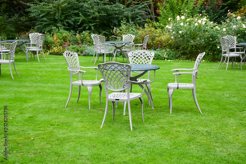 Garden party, table and chairs set out on lawn of Public park ready for customers to enjoy coffee , tea and cakes from the cafe on a sunny day.