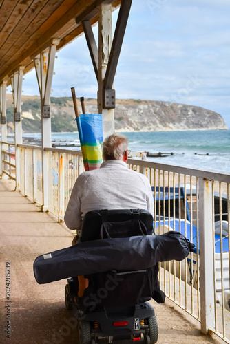 Man on a mobility scooter taking his chair and windbreak to the beach in Swanage UK able to enjoy a day on the beach despite his disability as the vehicle allows him to be independent and travel freel