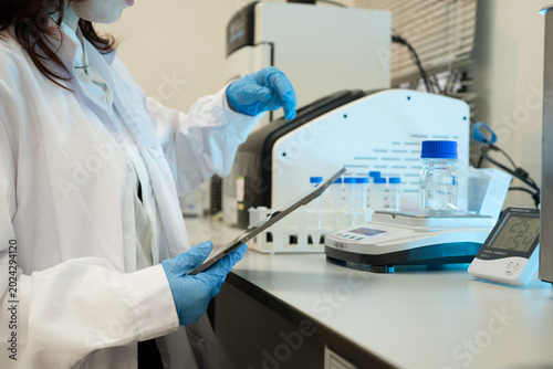 Female Scientist in Lab Coat and Blue Gloves Handling Sample in Professional Laboratory Setting