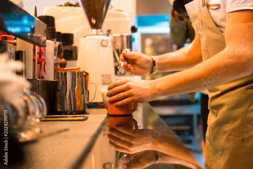 Quadro su tela A skilled barista expertly pours steamed milk into a cup, crafting a specialty coffee drink in a bustling cafe environment