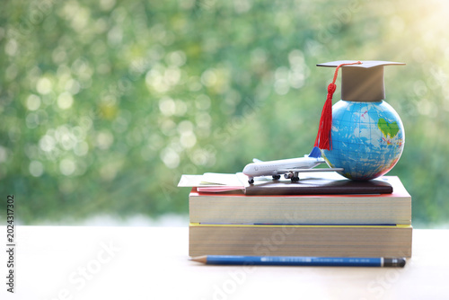 Graduation cap on globe with airplane model and passport on books, symbolic of international education, study abroad planning, global scholarship, and career success on green bokeh background.