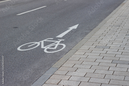 Schilderij op canvas Bicycle lane marking on asphalt road with directional arrow and adjacent paved s