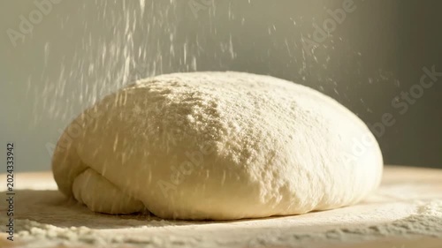 A smooth, rounded piece of dough on a floured surface with flour being sprinkled