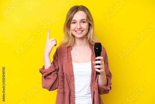 Foto Young singer caucasian woman picking up a microphone isolated on yellow backgrou