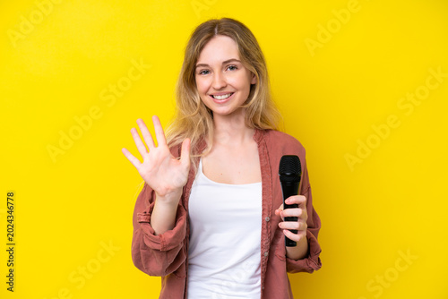 Photos Young singer caucasian woman picking up a microphone isolated on yellow backgrou