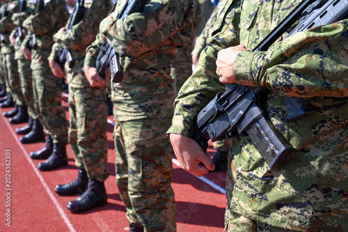 Soldiers standing in formation holding rifles at military barracks. Military parade with armed soldiers in uniform. Group of soldiers holding automatic riffles.