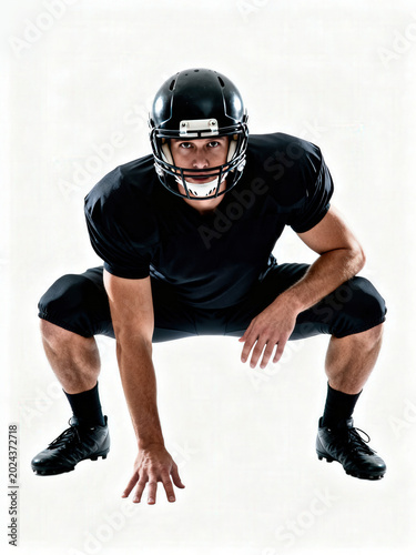 Intense football player in black uniform crouching in a three-point stance on white background.