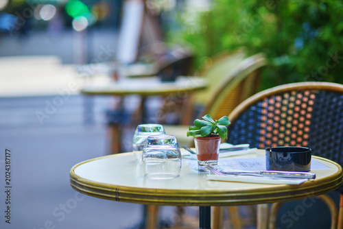 Obraz na płótnie Empty outdoor cafe table on a quiet Paris street with upside-down glasses, cutlery, an ashtray, and a small potted succulent