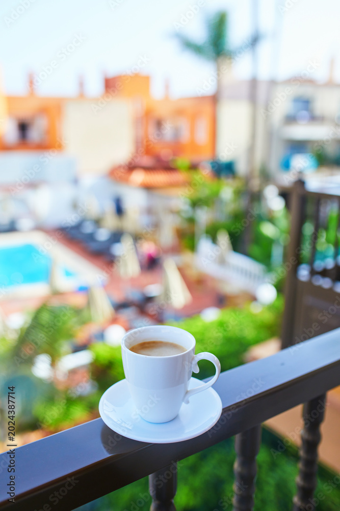 Obraz premium Cup of coffee on a hotel balcony overlooking a swimming pool and tropical courtyard in Tenerife, Canary Islands, Spain.