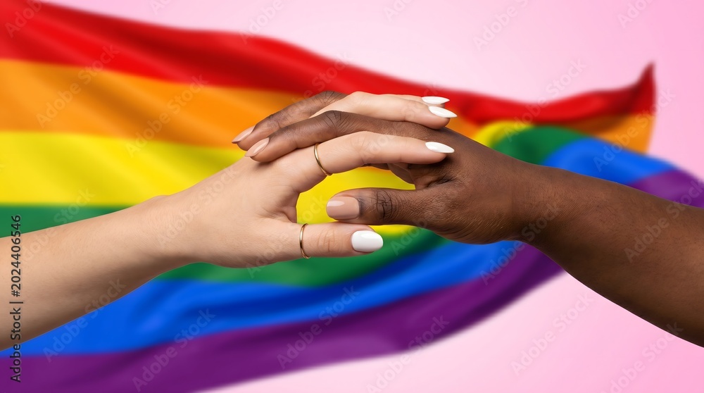 Fototapeta premium Two diverse hands gently touch, symbolizing love, unity, and support for the LGBTQ+ community, set against a blurred pride flag and soft pink background
