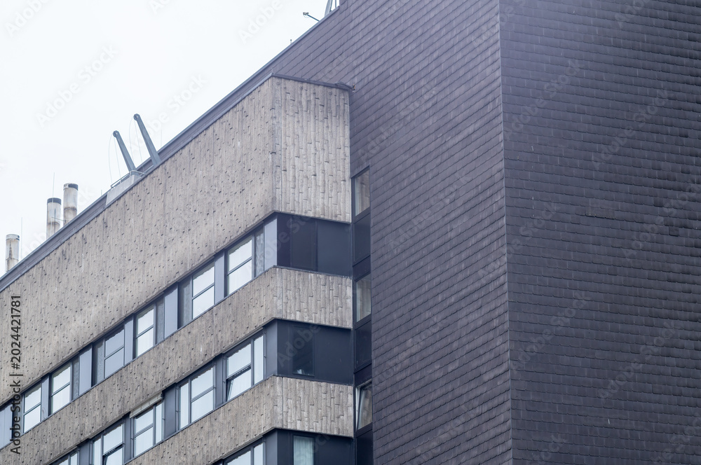 Obraz premium Building corner with windows and panels under cloudy sky in urban area during daytime