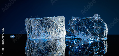 Cuadro en lienzo Broken ice with blue backlight on a black reflective background.