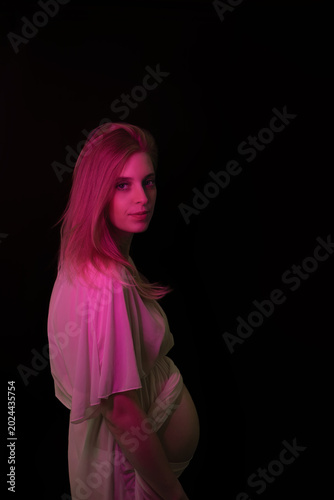 Low key photo of posing young pregnant woman illuminated by pink fluorescent light. Vertical. 