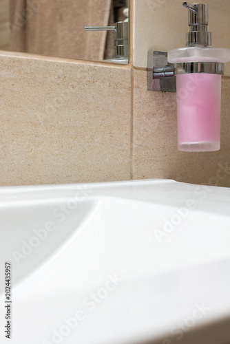 Closeup view of bathroom sink with liquid soap dispenser with reflection in mirror. Vertically.