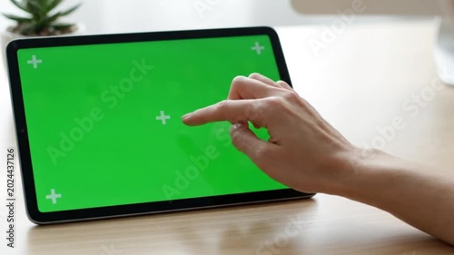 Hand using a digital tablet with a green screen on a wooden desk