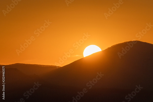 Sunrise over rolling hills with golden sunlight illuminating the landscape, creating a serene and tranquil atmosphere in the early morning sky