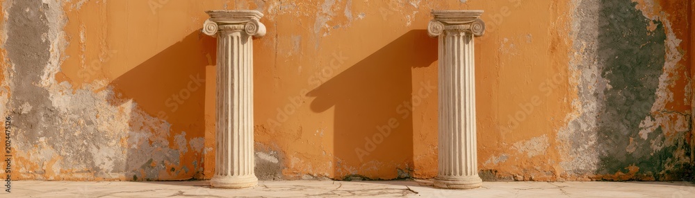 Naklejka premium Two classical stone columns standing before textured orange weathered plaster wall surface