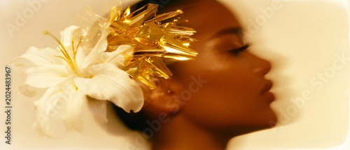 Surreal fashion portrait of a woman with a golden abstract accessory and white flower