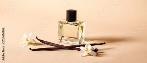 Elegant perfume bottle with vanilla pods and delicate white flowers on beige