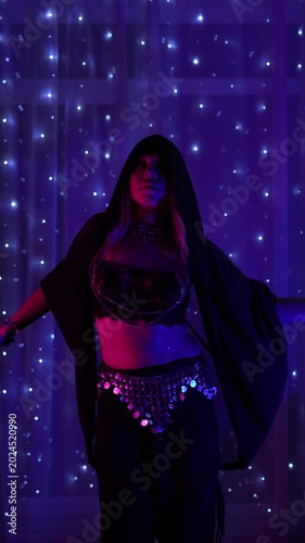 Young woman performs belly dance with flowing arm and body waves. Graceful oriental choreography in purple neon light creates a mystical, sensual and hypnotic stage atmosphere
