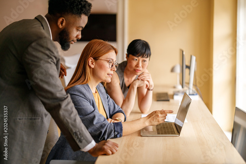 Businesswoman pointing at laptop while collaborating with team during brainstorming meeting in workplace
