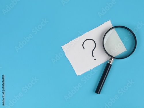 Fotografía Question mark on a piece of white paper with magnifying glass on blue background