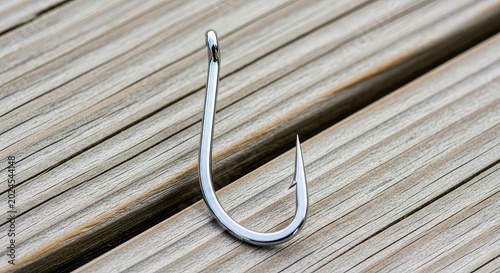 Close-up view of a shiny steel fishing hook with a sharp point and barb, resting on a textured wooden dock ready for outdoor angling gear, recreation, accessory, survival