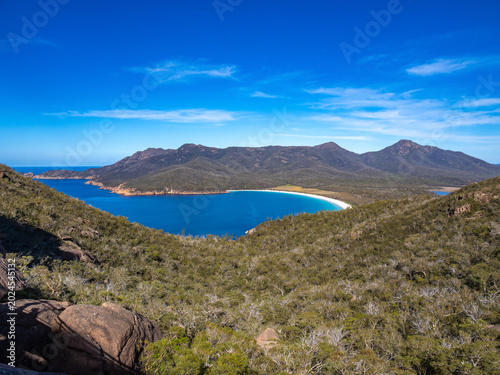 Wineglass Bay, a crescent-shaped beach with white sands and turquoise waters framed by the Hazards granite peaks. Freycinet National Park Tasmania, Australia