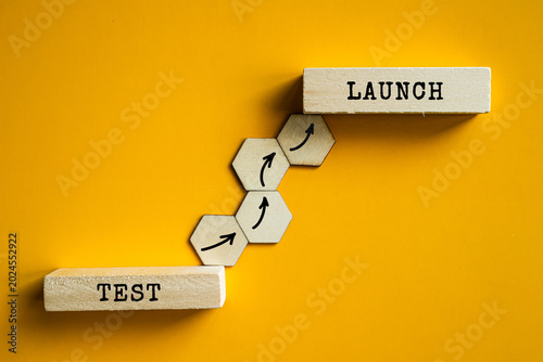 Test and Launch wooden labels with hexagon steps on orange background, software development and product release management concept