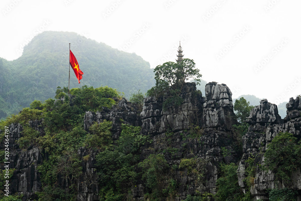 Naklejka premium Vietnamese flag above limestone cliffs in Ninh Binh Vietnam