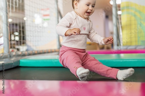 Happy toddler girl jumping on trampoline in indoor playground